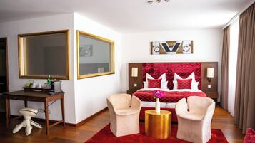 A hotel room with a large bed, two armchairs, a desk, and a mirror.
