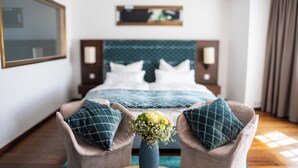 Ein Hotelzimmer mit einem Bett, zwei Sesseln, einer Blumenvase, einem großen Spiegel und einem Wandregal.
