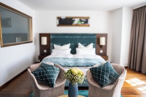A hotel room with a bed, two armchairs, a vase with flowers, a large mirror, and a wall-mounted shelf. - Luxury Boutique Hotel Iris Porsche (Mondsee)