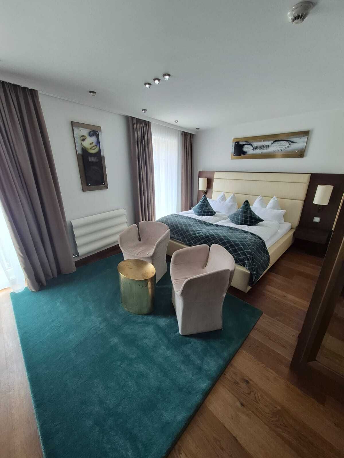 Et hotelværelse med en seng, to lænestole, et rundt bord og et billede på væggen.