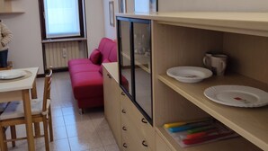 Eine kleine Küche mit Esstisch, Stühlen, einem roten Sofa und einem Schrank mit Regalen.