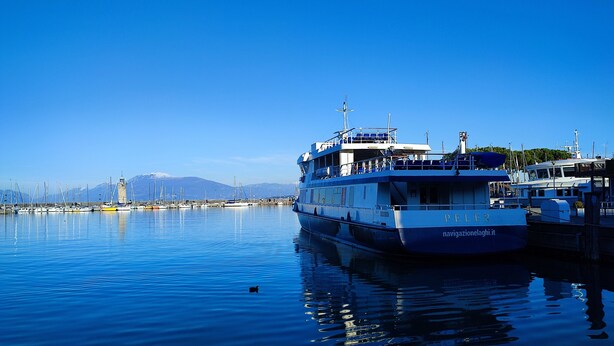 Eine große Fähre liegt in einer Marina vor Anker, mit blauem Himmel und Bergen im Hintergrund.
