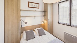 Un dormitori amb llit, abacines, armari, finestra amb cortines i una prestatgeria penjada a la paret.