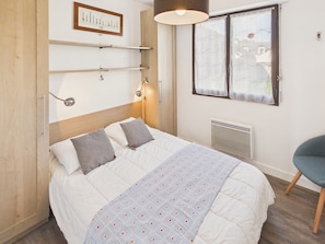 Un dormitorio con cama, mesita de noche, lámpara, ventana con cortinas y radiador.