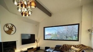 Een moderne woonkamer met een grote flatscreen televisie, een open haard, een leren bank en een kroonluchter.