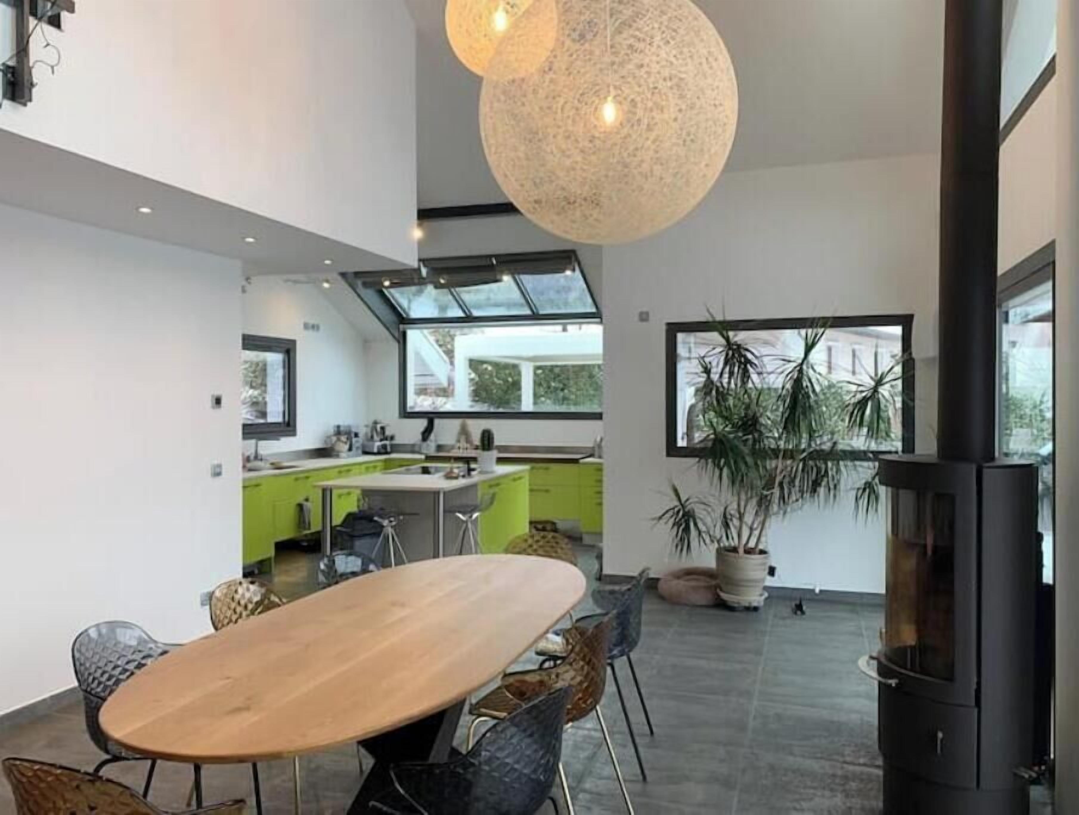 Una cocina moderna con una isla grande, un comedor con mesa y sillas de madera, y una lámpara colgante de gran tamaño.