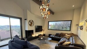 Een moderne woonkamer met een open haard, een groot raam, een bank en een relax fauteuil.