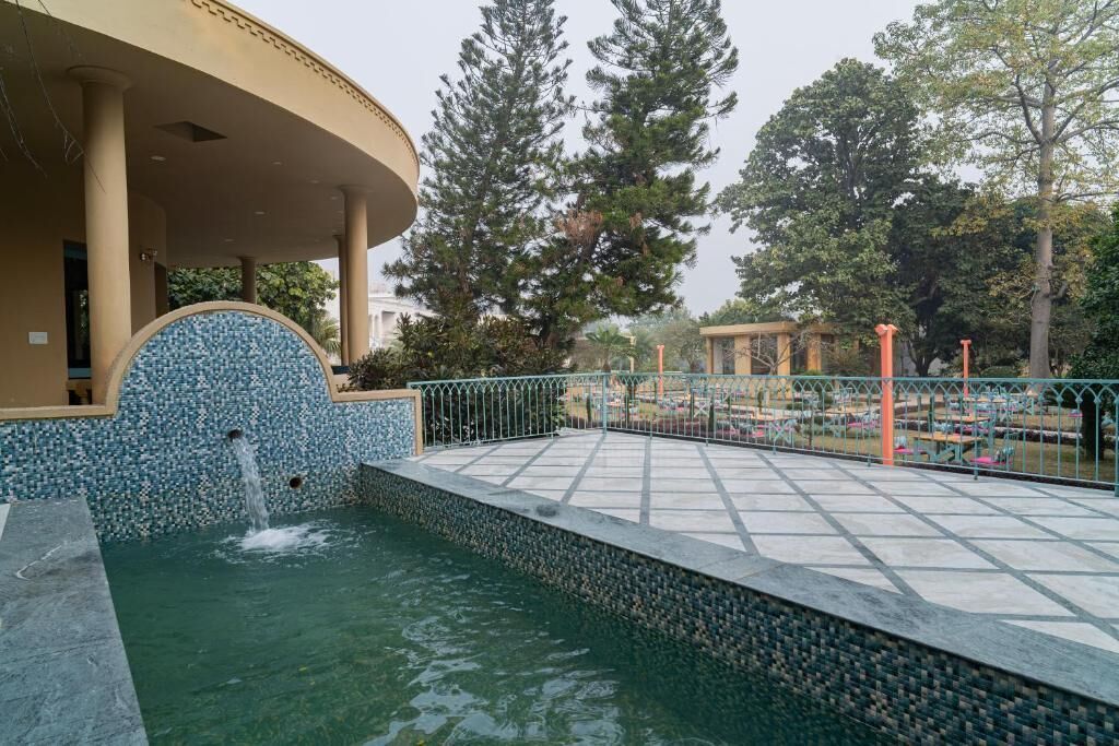 Un área de piscina con solárium empedrado, una fuente y una zona de estar cubierta.