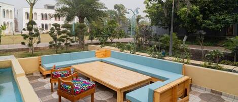 A poolside area with a wooden bench and chairs, a small table, and a pool.