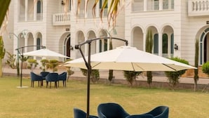Un espace extérieur aménagé avec des chaises et des parasols bleus, et un bâtiment blanc avec des arcades en arrière-plan.