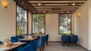 Un espace repas avec des tables et des chaises, de grandes fenêtres et des poutres en bois au plafond.