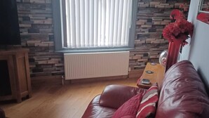 A living room with a leather sofa, a wooden coffee table, a radiator, and a window with blinds. - 1 Apartment Sleeps 2 (Sutton-in-Ashfield)