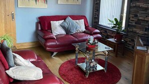 A red leather sofa with cushions, a glass coffee table with decorative items, a red rug, and a potted plant. - 1 Apartment Sleeps 2 (Sutton-in-Ashfield)