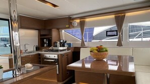 A modern kitchen with a central island, a dining area with a table, and a view through the windows. - Sun-Kissed Sailing Adventure in Islas Sarónicas (Alimos)