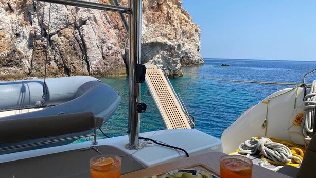 A boat with a table set for two, a plate of sliced vegetables, and two drinks. - Sun-Kissed Sailing Adventure in Islas Sarónicas (Alimos)