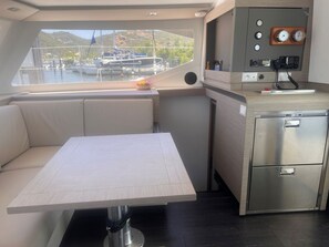 Une cuisine compacte comprenant un coin repas, un petit réfrigérateur et une fenêtre donnant sur les bateaux et les collines.
