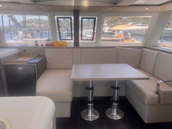 Interior de un barco con una zona de estar con cojines, una mesita y un armario.