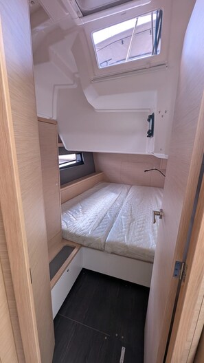 Ein kompaktes Wohnmobil-Innenraum mit einem Schlafplatz, einem Dachfenster, einem kleinen Fenster und einer eingebauten Sitzbank.