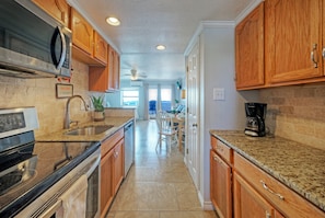 A kitchen with wooden cabinets, a microwave, a stove, a sink, and a coffee maker. - Steps to Beach + Boardwalk | 2 Pools + Pickleball Access | Gulf View Efficiency (Port Aransas)