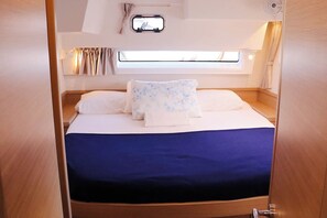 A compact, well-lit room with a bed, a small window, and a wall-mounted control panel.
