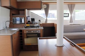 A compact kitchenette with a microwave, stove, and oven, a sink, and a window with curtains.