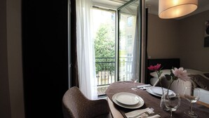 Hotellihuone, jossa on ruokapöytä kahdelle, parveke, jolta on näkymä, ja sänky päätyosalla.