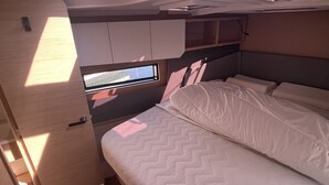 Une pièce compacte et bien éclairée, comprenant un lit, une petite fenêtre et un téléviseur encastré.