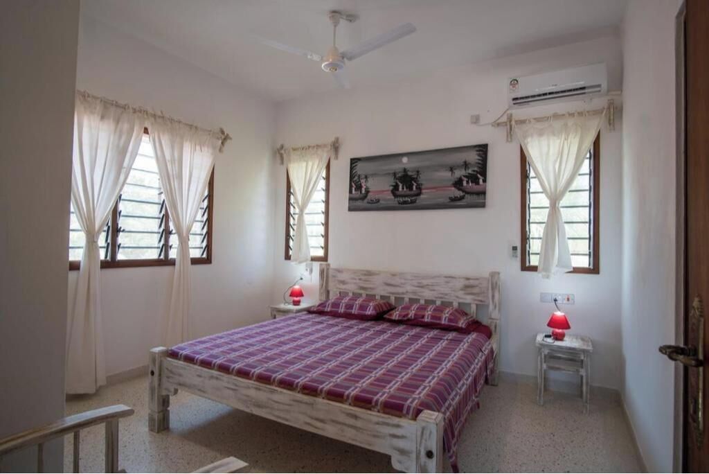 Een slaapkamer met een bed, twee nachtkastjes, een plafondventilator, een airconditioning en een schilderij aan de muur.