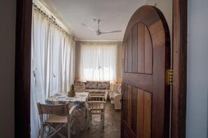 A room with a dining table, chairs, a sofa, a ceiling fan, and a wooden door. - Casa Di Philo 2 – Elegant Coastal Escape in Watamu with Pool & Garden (J2XF+F9P, Watamu)