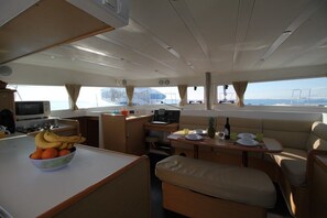 A compact galley with a stove, a small sink, a dining area with a table and chairs, and a seating area with a cushioned bench. - Sun-Kissed Sailing Adventure in Islas Sarónicas (Alimos)