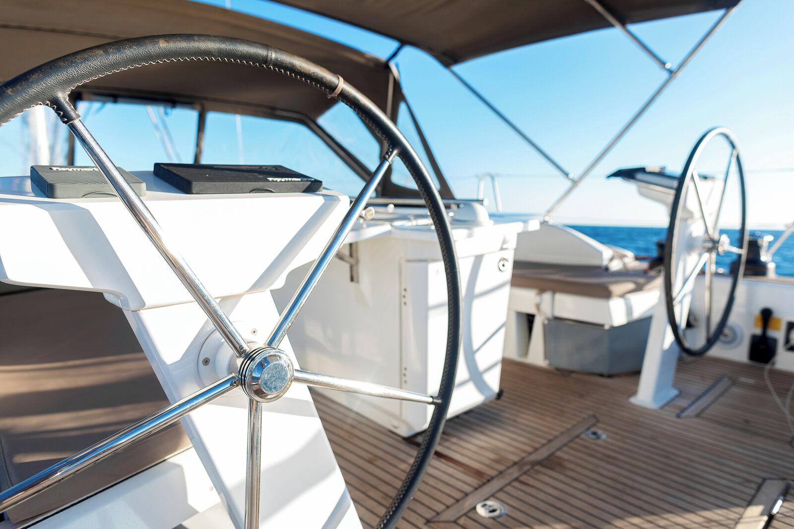 A boat's steering wheel, part of the deck, and a glimpse of the ocean.