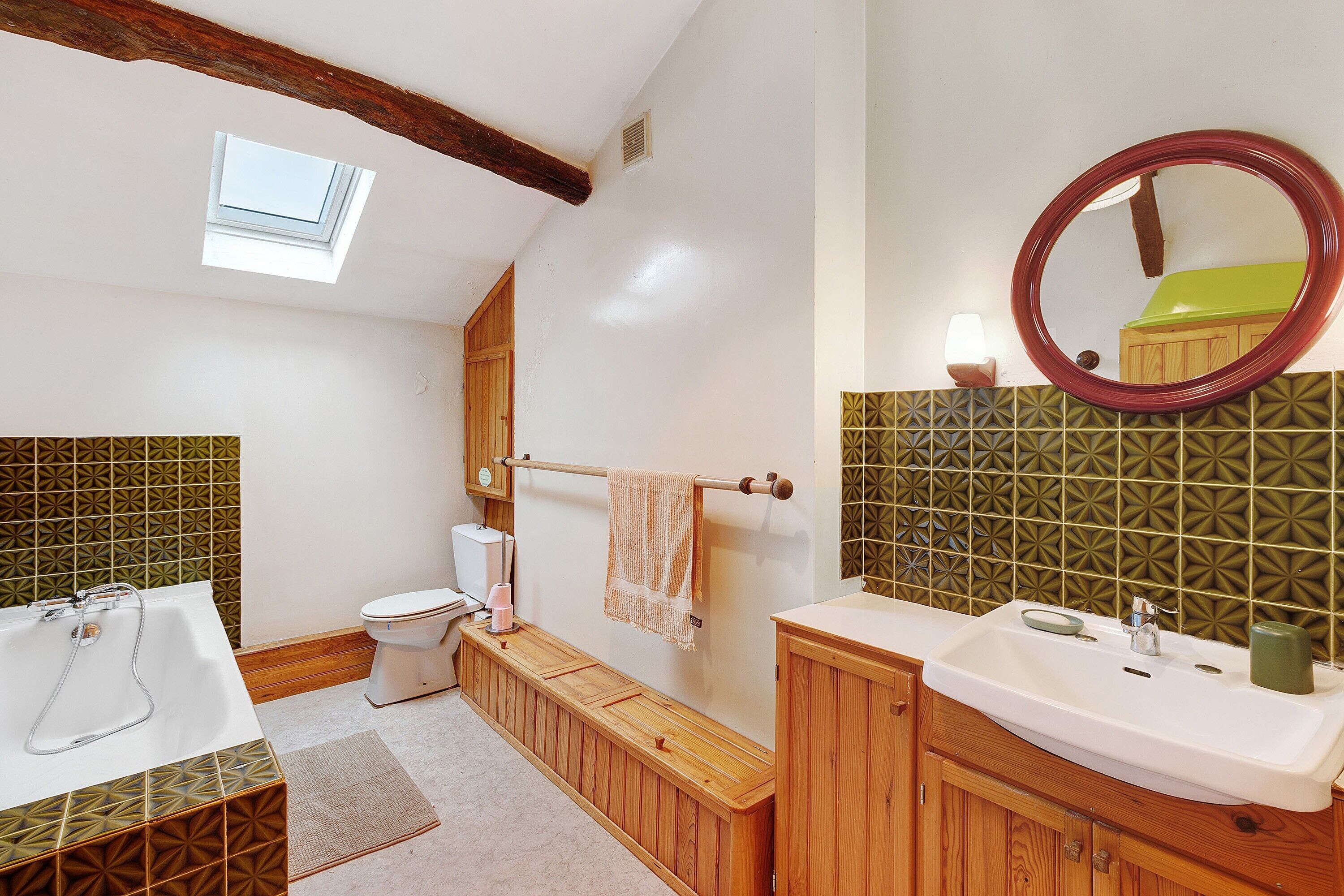 A bathroom with a bathtub, toilet, vanity, and a skylight.