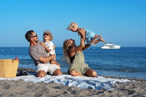 Eine Familie am Strand mit einem Picknickkorb und einem Boot im Hintergrund.