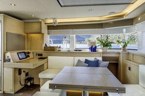 A modern interior with a dining area, seating, a control panel, and large windows offering a view of the water. - Sun-Kissed Sailing Adventure in the Saronic Islands (Elliniko)