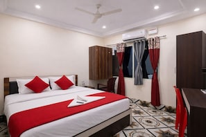 A hotel room with a bed, a desk, a wardrobe, a ceiling fan, and an air conditioning unit. - Hotel Atrangi Waves Near Golden Beach (Puri)