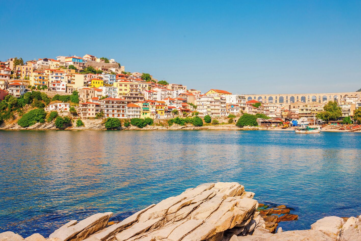 A coastal town with colorful buildings, a clear blue sky, and a rocky shoreline.