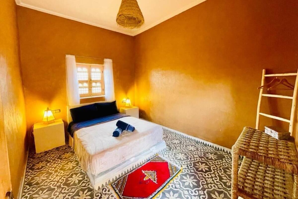 Una habitación con cama, mesita de noche, lámpara colgante y suelo estampado.