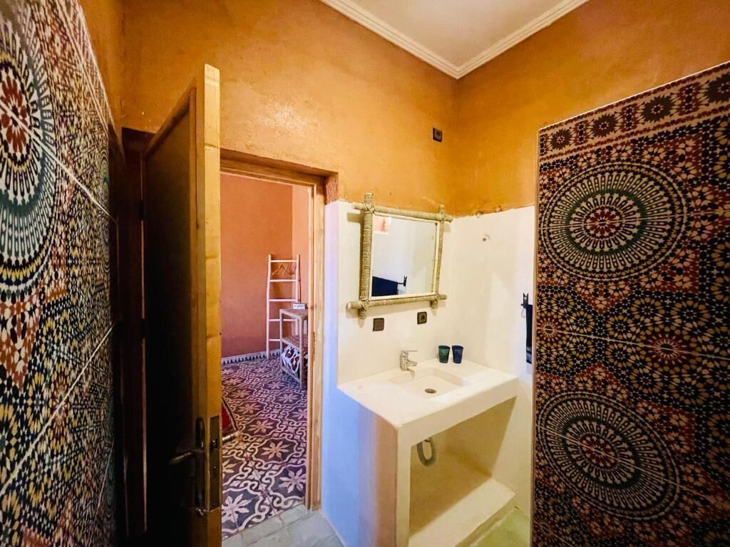 A bathroom with a white sink, a mirror, patterned walls, and a door leading to another room.