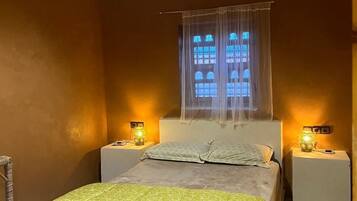 Ein Schlafzimmer mit einem Bett, zwei Nachttischen mit Lampen, einem Fenster mit Vorhängen und einem gemusterten Teppich.