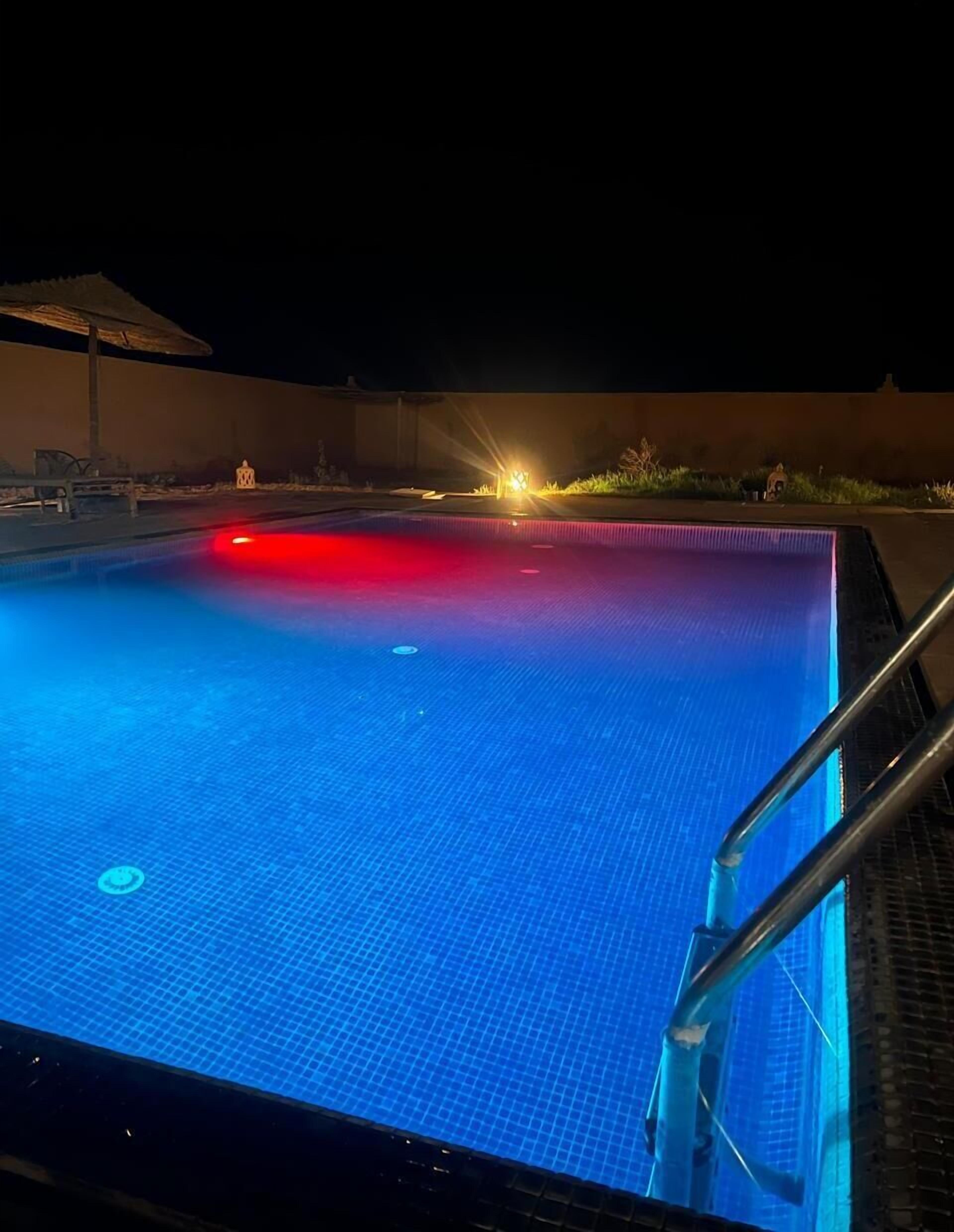 A swimming pool with a blue tiled floor, a red light on the left side, and a metal ladder on the right.