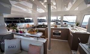 A modern yacht interior with a dining area, kitchen, and seating space.