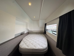 A compact, single-bed room with a window, a headboard, and a small bedside table.
