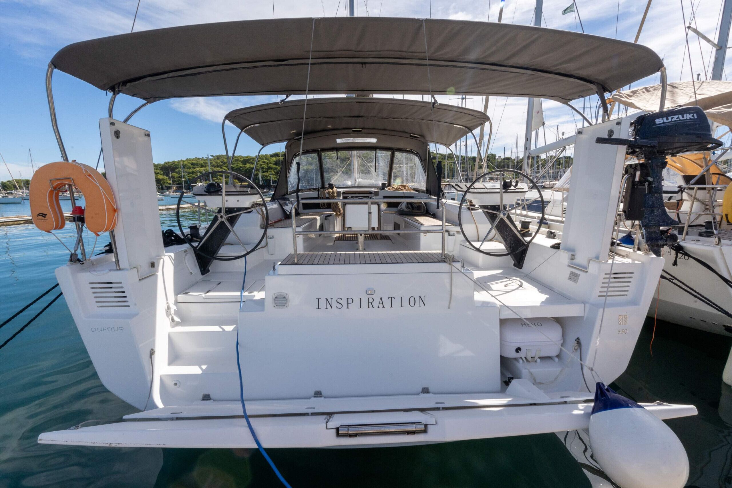 A sailboat named 'Inspiration' docked at a marina with other boats, a life buoy, and a Suzuki outboard motor.