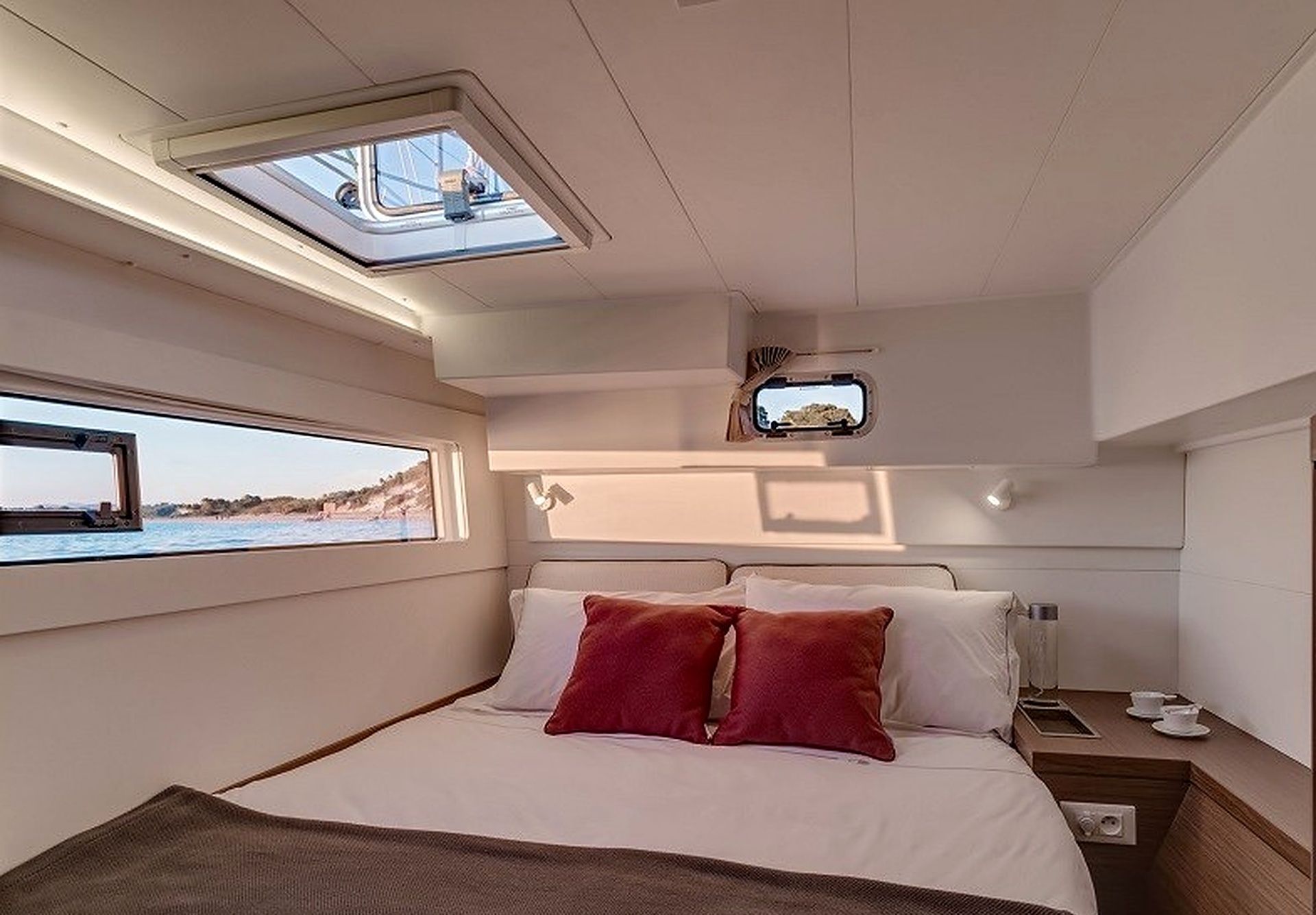 A bedroom with a bed, a skylight, a television, and a window with a view of the sea.
