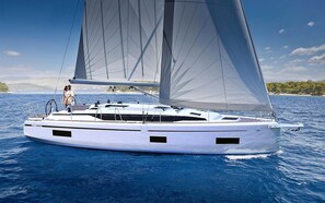 A white yacht with multiple sails on the water, a person on deck, and a coastline in the background.