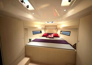 A compact, well-lit room with a bed, two monitors, and a small plant.