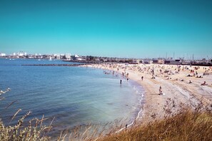 A beach with people, a pier, and buildings in the background. - Sun-Kissed Sailing Adventure in Antiguo Puerto de La Rochelle (La Rochelle)