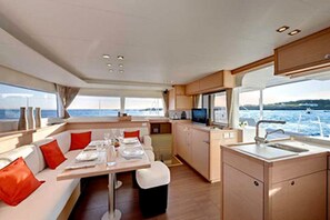 A modern interior with a dining area, kitchen, and seating by a window overlooking the sea.