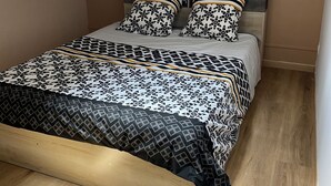 Een slaapkamer met een schuine balklaag, een bed met behangdessin, een bedlamp en een airconditioner.