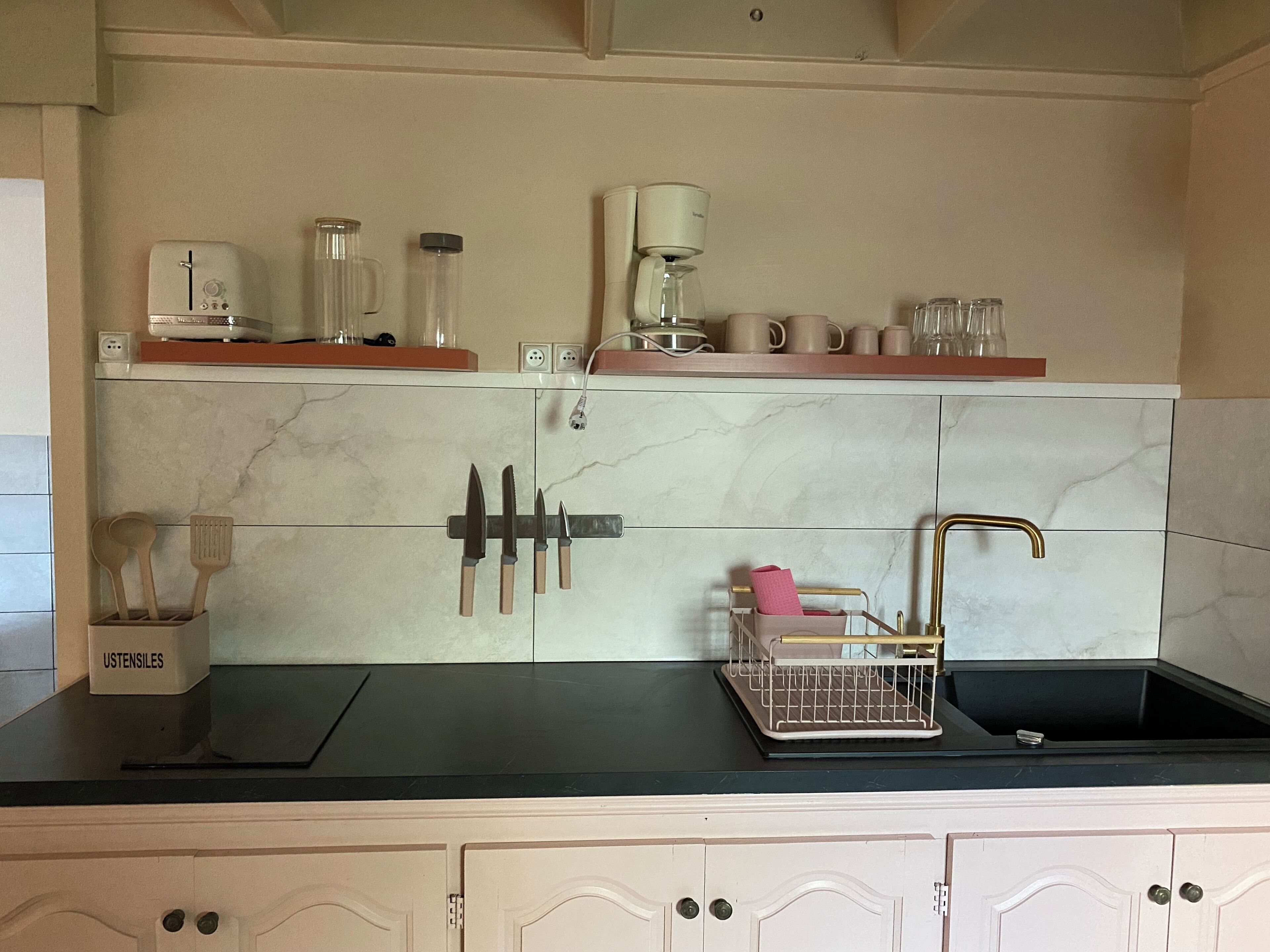 Een keuken met een marmeren achterwand, een messenblok, een koffiezetapparaat en een gootsteen met een handdoekhouder.